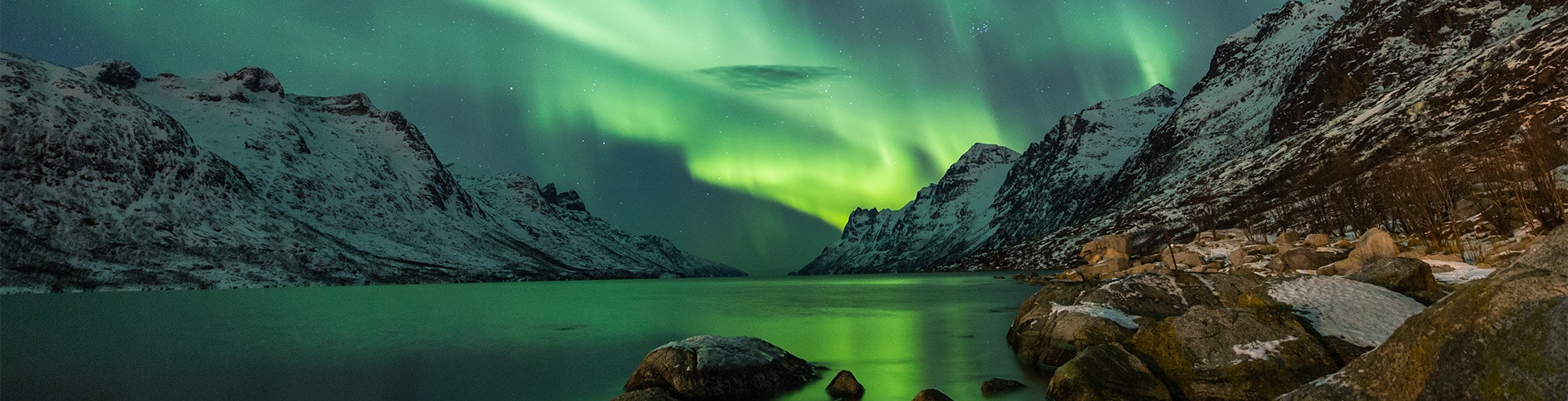 Green northern lights dancing above a lake in Iceland with a mountain range in the background